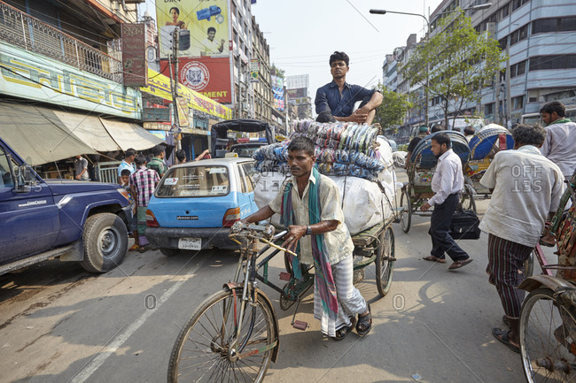 Dhaka, Bangladesh - April 27, 2013: Cycle-rickshaw driver pulling his heavy rickshaw with a man sitting on it on busy street