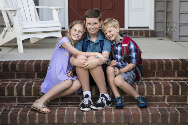 Three Smiling Siblings Sit on Brick Front Porch Steps