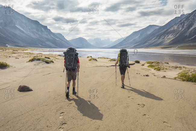 Rear view of two backpackers hiking, leaving footprints in the sand.