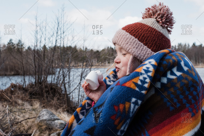 Young girl wrapped in a blanket eating a marshmallow while camping