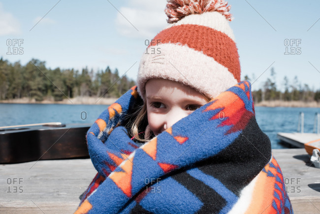 Young girl wrapped up in a blanket by the lake keeping warm