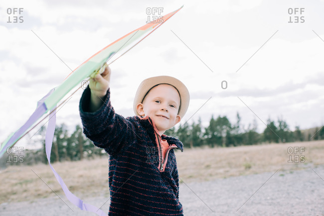 Young boy holding a kite smiling whilst outside on a sunny day