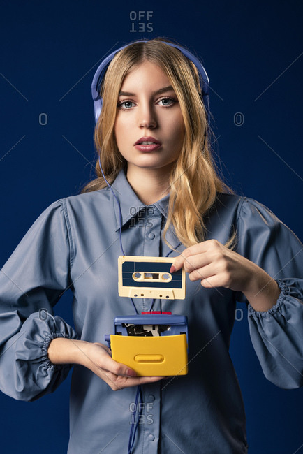 Young blond woman with portable music device and headphones in front of blue background
