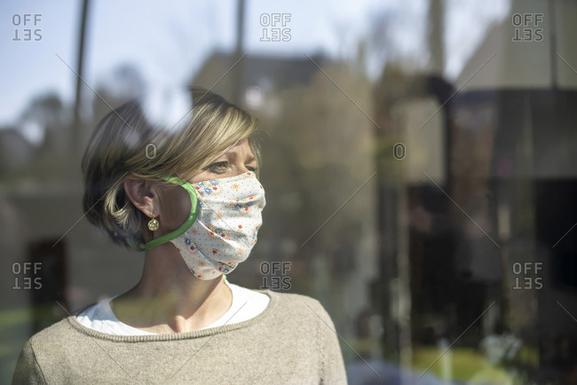 Woman wearing floral mask while looking away through window during isolation
