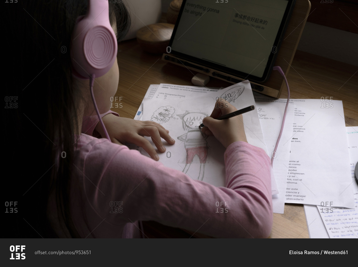 Girl wearing headphones drawing manga comics while using digital tablet at desk in house