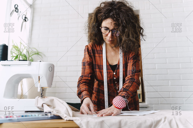 Woman pinning sewing pattern on table at home