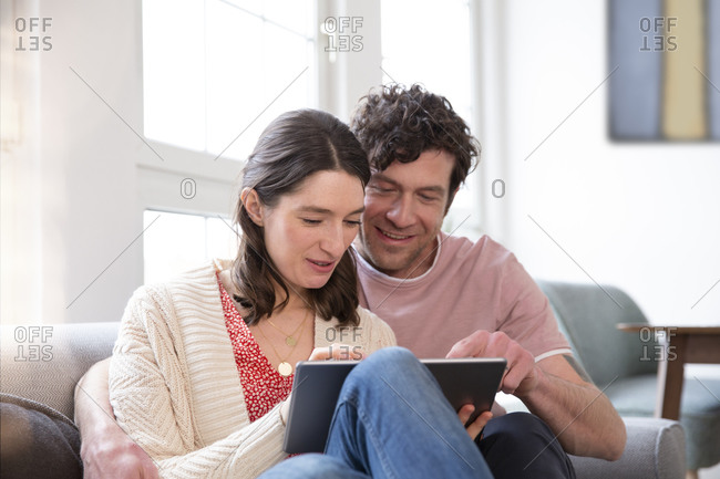 Couple sitting on couch at home using tablet