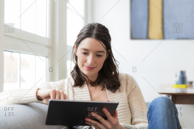 Woman sitting on couch at home using tablet