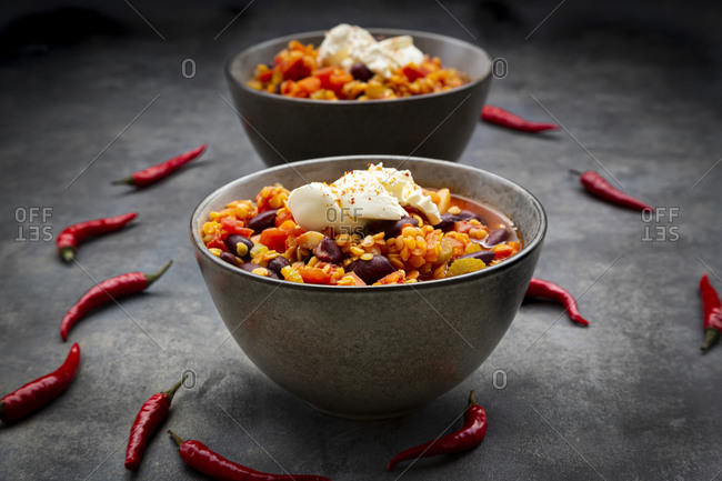 Red chili peppers and two bowls of vegetarian chili with red lentils- kidney beans- tomatoes- carrots- celery and sour cream