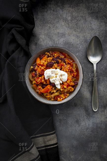 Bowl of vegetarian chili with red lentils- kidney beans- tomatoes- carrots- celery and sour cream