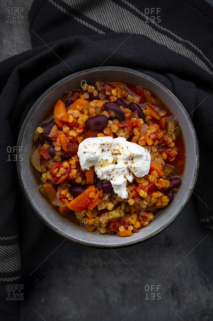 Bowl of vegetarian chili with red lentils- kidney beans- tomatoes- carrots- celery and sour cream