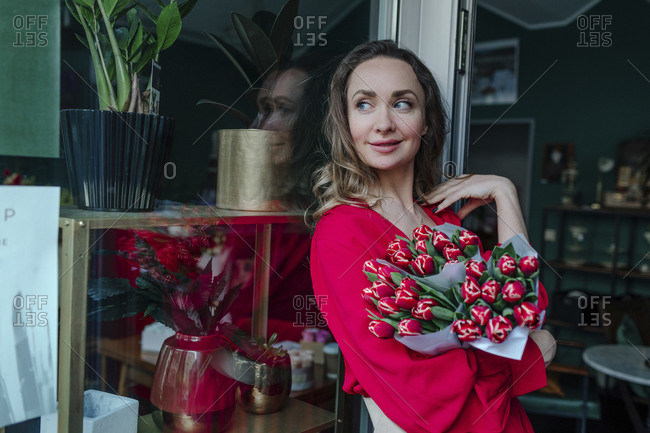 Smiling woman with a bouquet of flowers at the window in a flower shop
