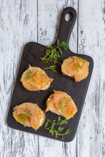 Baguette slices with dill and salmon meat on wooden cutting board