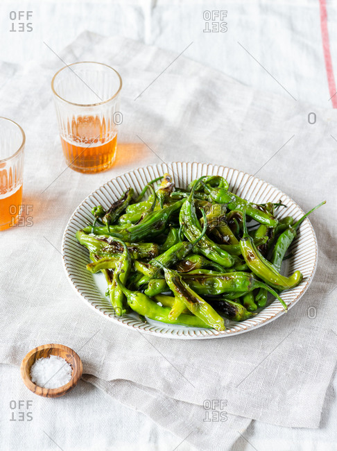 Fried shishito peppers (padron peppers) on a plate with glasses of beer