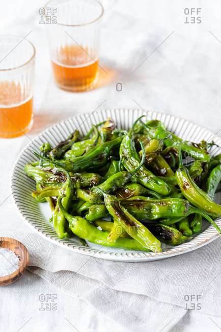 Fried shishito peppers (padron peppers) on a plate with glasses of beer