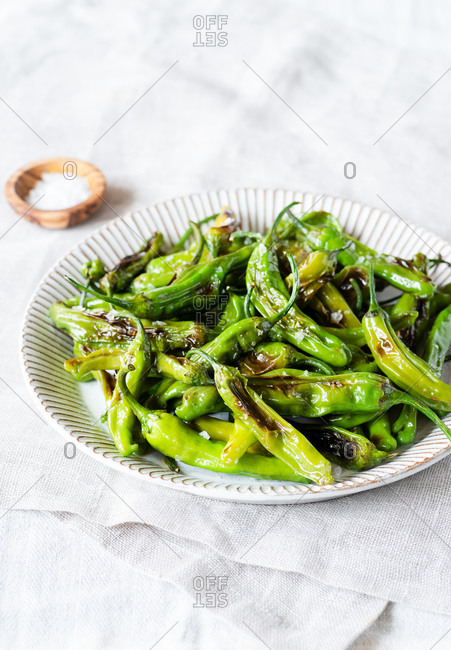 Fried shishito peppers (padron peppers) on a plate, salt on the side