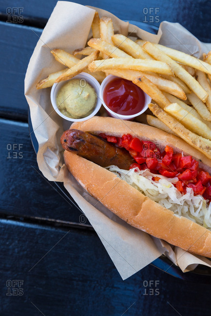 A hotdog with sauerkraut and red pepper relish with a side of fries, ketchup and mustard
