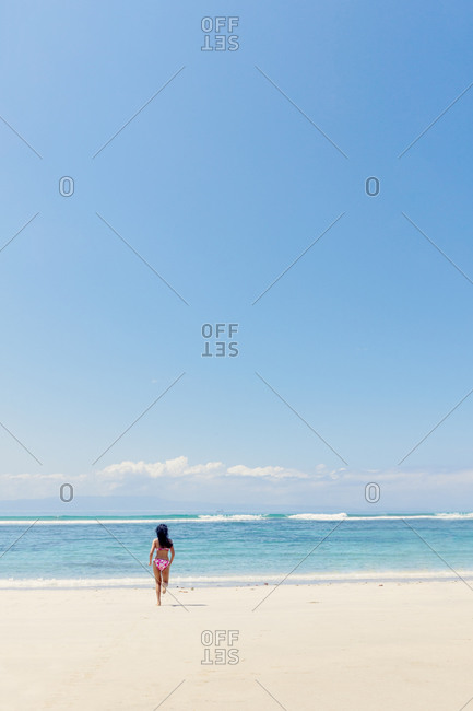 A young woman running into the ocean on a pristine tropical beach, Bali, Indonesia, Southeast Asia, Asia