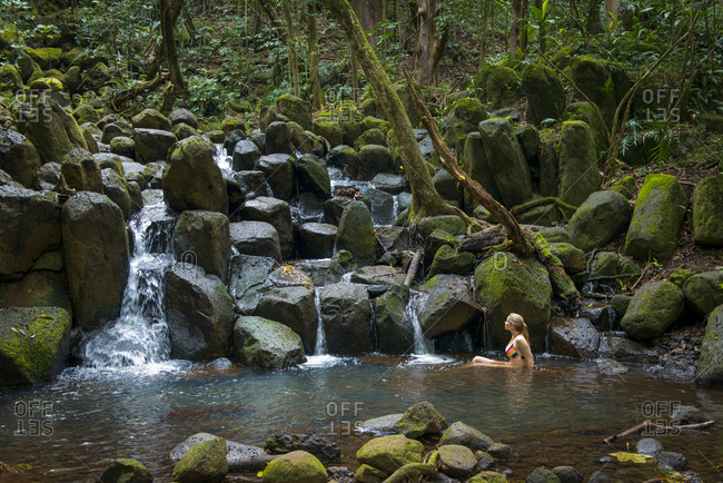 April 20, 2014: Woman lounging in a pool beneath a waterfall in Kauai, Hawaii, United States of America, North America