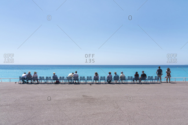 June 1, 2018: Line of people on chairs looking out to the sea, Nice, Alpes Maritimes, Cote d'Azur, French Riviera, Provence, France, Mediterranean, Europe