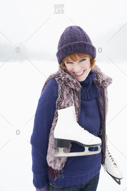 Italy- South Tyrol- Seiseralm- Young woman on frozen lake carrying ice skates- smiling- portrait