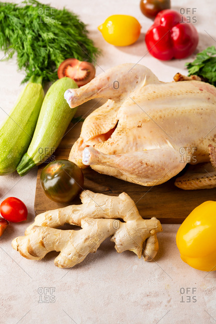 Whole uncooked chicken and vegetables on cutting board