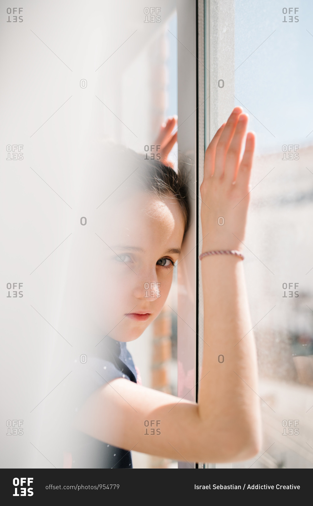 Side view of sad girl standing near window with hands on glass