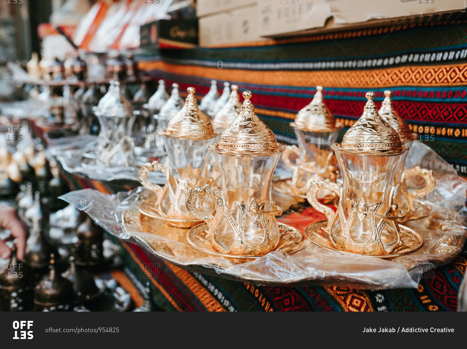 Set of glass traditional Turkish teapots with golden ornaments composed on tray on patterned oriental fabric at market in Istanbul