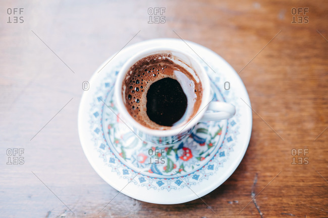From above of aromatic black hot Turkish coffee in fragile traditional white cup and saucer painted with oriental pattern standing on wooden table