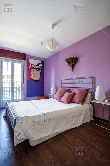 Comfortable steal bed on bright purple wall in modern studio apartment decorated in minimalist style