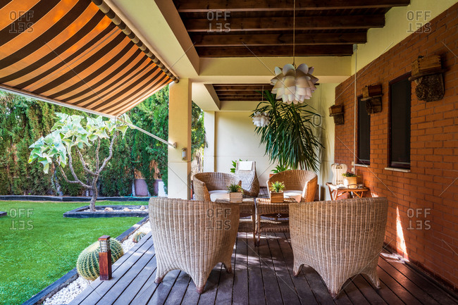 Wooden table with chairs placed on spacious garden terrace of modern country house surrounded with green plants