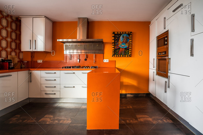 Contemporary kitchen interior with bright orange wall and counter decorated with picture in ethnic style in modern apartment