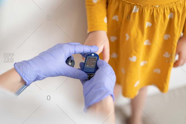 From above view of anonymous doctor in latex gloves using finger cuff to examine blood pressure of little girl in casual yellow dress