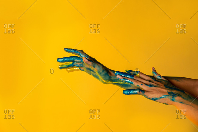 Unrecognizable crop female artist with hands painted in metallic yellow and blue paint