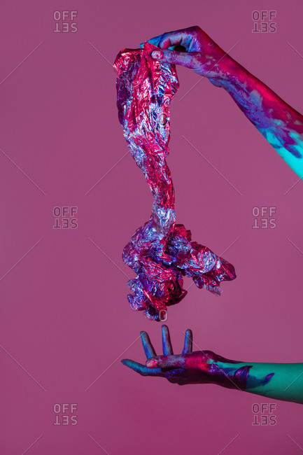 Unrecognizable female with painted hands holding piece of aluminum crumpled foil on violet background in studio