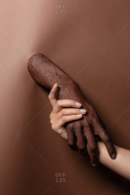 Unrecognizable crop multiethnic couple holding hands while standing behind paper curtain