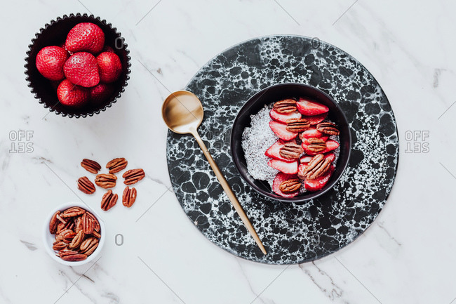 Top view of yummy sorbet with fresh strawberries and walnuts served in bowl on marble table near spoon