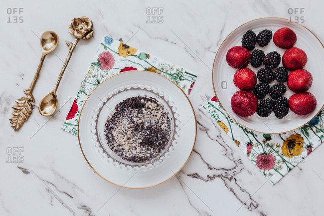 Bowl with delicious poppy seed pudding and plate with strawberries and blackberries placed near paper napkins and ornamental spoons on marble table