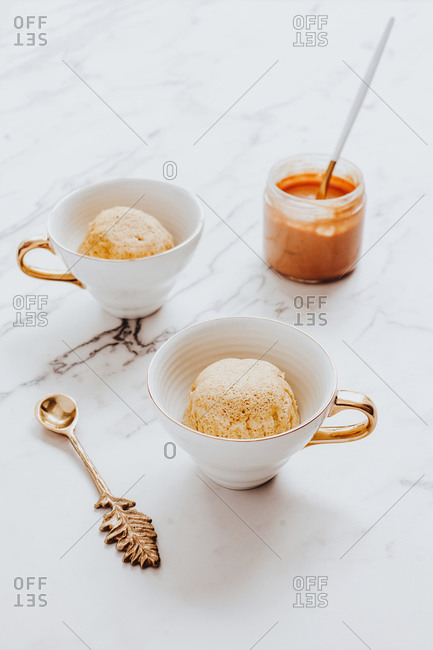 Cups with ice cream bowls placed near ornamental spoon and jar of peanut butter on marble table
