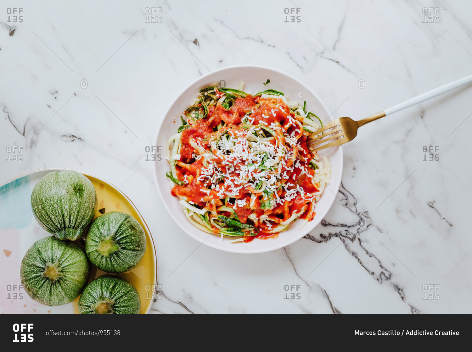 From above delicious healthy mix of fresh green pasta made of round zucchini with tomato sauce and topped with grated cheese place on marble surface with fork