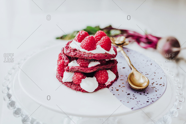 High angle of delicious organic beet pancakes with fresh raspberry on plate with golden spoon on white table