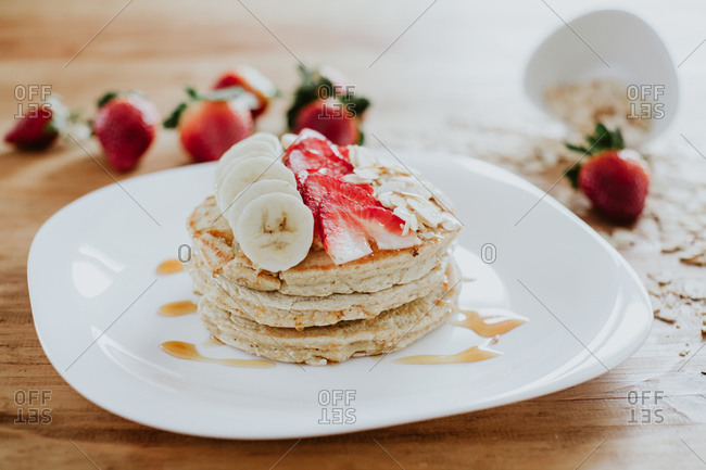 Closeup stack of yummy pancakes with pieces of banana and strawberry served on plate with almond flakes and honey during breakfast