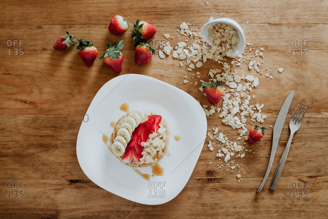 Stack of tasty pancakes served on plate with pieces of banana and strawberry and fresh blueberries with coconut flakes during breakfast