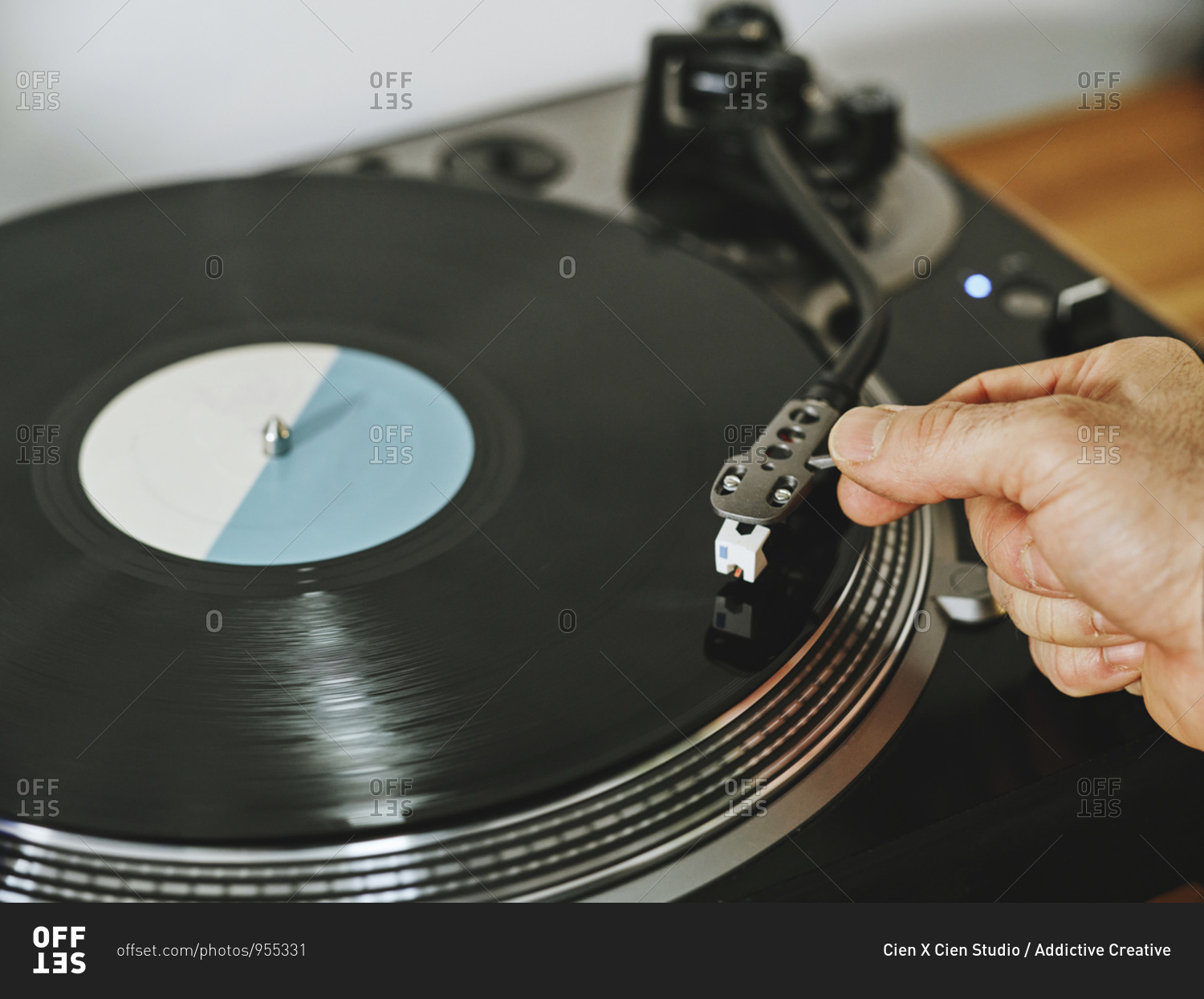 From above cropped person hands adjusting a contemporary vinyl record player with retro disc placed on wooden table