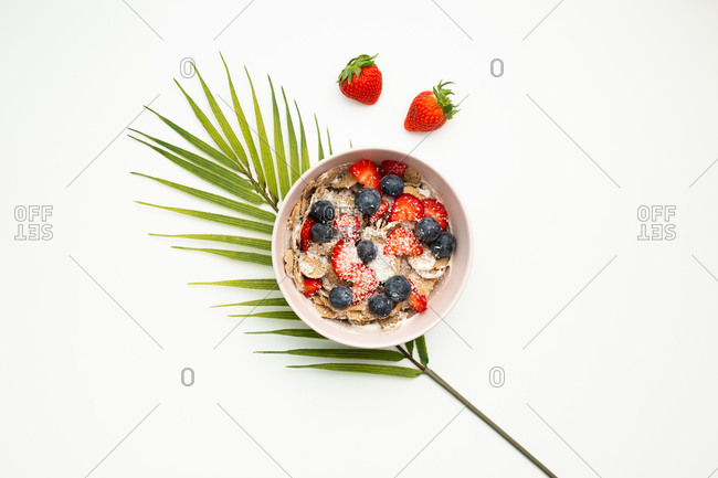 Top view of delicious dish with strawberries and blueberries placed on top of palm leaf