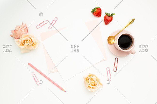Top view of blank paper and stationery placed on white desk with hot espresso and rose buds as decoration