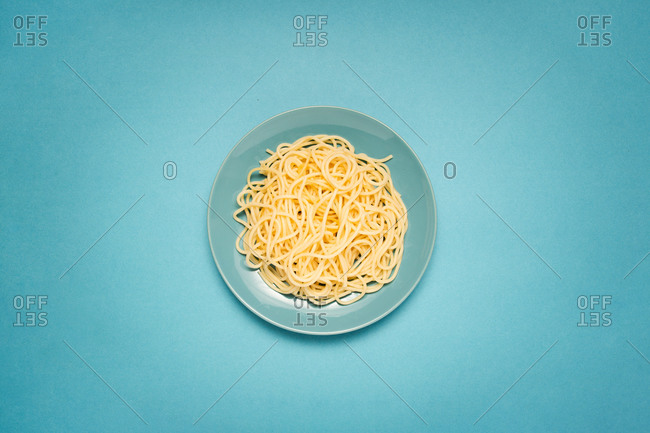 From above of blue ceramic plate with homemade cooked pasta on bright blue background