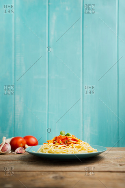 Blue ceramic plate with pasta and tomato sauce decorated with parsley on a wooden table with light blue wooden background
