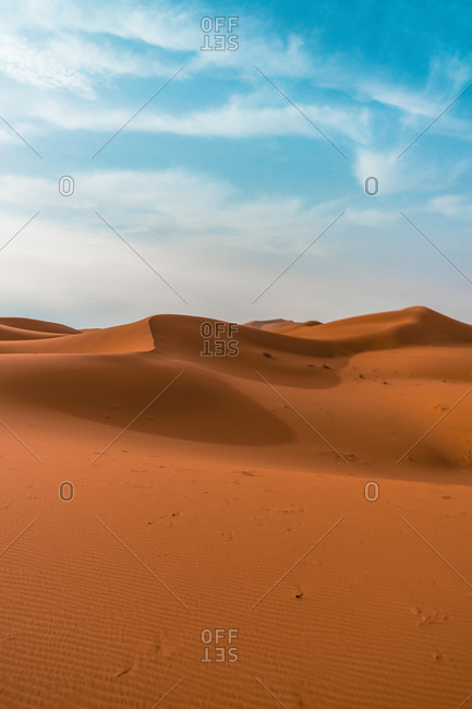 Minimalistic desert landscape with sandy dunes under blue cloudy sky in sunny day