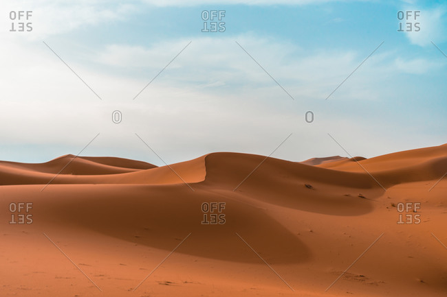 Minimalistic desert landscape with sandy dunes under blue cloudy sky in sunny day